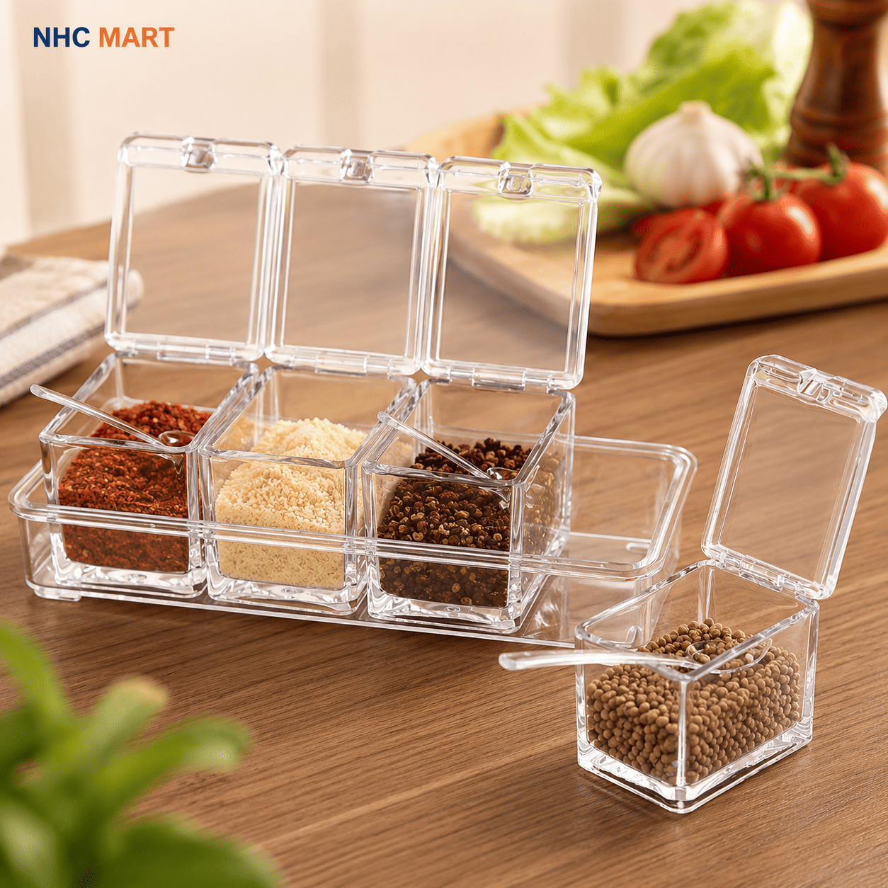 Clear plastic spice container set with six square compartments, shown open on a wooden table with various spices inside. One container is detached and placed in front with its lid open.