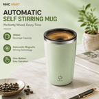 A pale mint green automatic self-stirring mug with a stainless steel rim, shown on a marble tabletop with coffee beans, a pen, and a plant in the background. The left side features product feature callouts with the NHC MART brand logo.