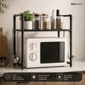 A 2-tier black metal kitchen organizer shelf holding a white microwave, spice jars, and a small potted plant, shown in a kitchen setting with product feature badges along the bottom.