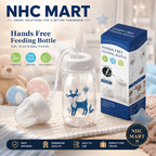 NHC Mart Hands Free Feeding Bottle set, featuring a 150ml clear baby bottle with a blue deer illustration, a white breast pump, and its blue retail packaging box, displayed on a cozy blanket with baby toys in the background.