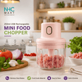 A pink mini food chopper with a clear jar filled with ground meat, shown on a kitchen countertop with tomatoes, onion, garlic, and herbs around it. The image includes marketing text and icons for features like USB rechargeability, one-touch operation, and food grade material.