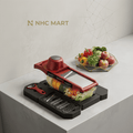 NHC Mart multi-functional vegetable slicer and dicer set in red and black, shown with various vegetables in a clear container on a kitchen counter next to a peeler and a bowl of fresh produce.