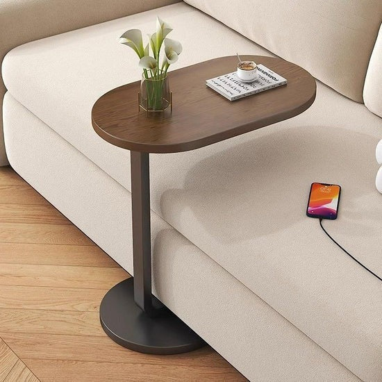 Small wooden side table with a vase of flowers and a smartphone on a beige sofa.