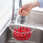 Person washing red berries in a metal mesh basket under running water from a faucet.