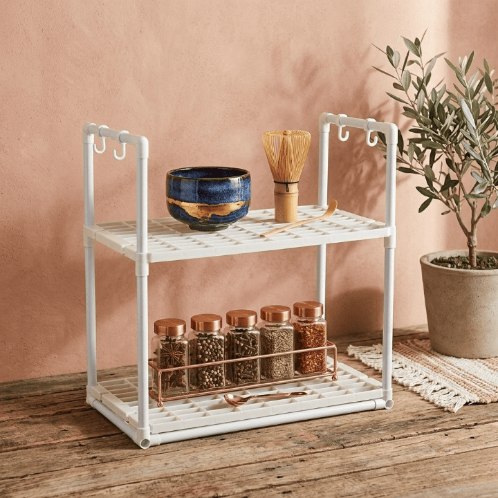 White metal rack with shelves holding kitchen items against a pink wall.