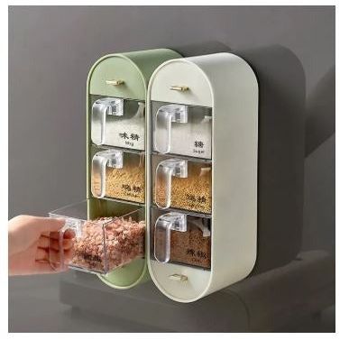 A wall-mounted spice rack with two cream-colored cabinets and six clear plastic spice jars with gold-tone handles. A hand is shown pulling out a jar of pink seasoning.